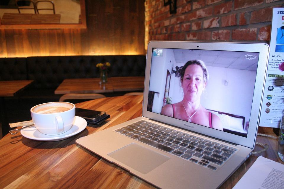 MacBook Air on a cafe table showing a Skype video call, with a coffee cup nearby