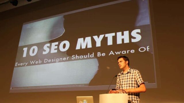 Presenter at a podium delivering a talk with a slide reading 10 SEO Myths Every Web Designer Should Be Aware Of