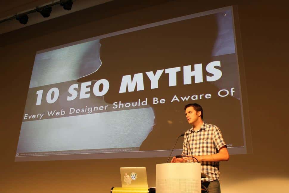 Presenter at a podium delivering a talk with a slide reading 10 SEO Myths Every Web Designer Should Be Aware Of