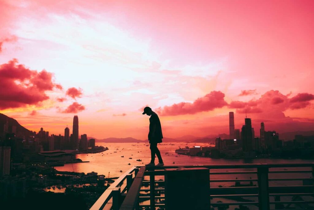 Silhouette of a person standing on a rooftop overlooking a city harbour at vivid pink sunset