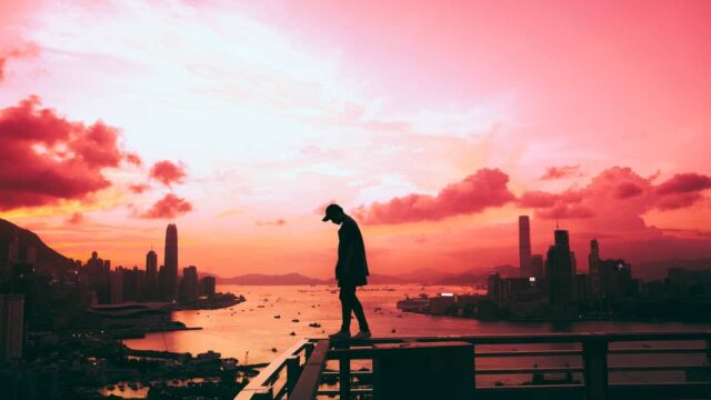Silhouette of a person standing on a rooftop overlooking a city harbour at vivid pink sunset
