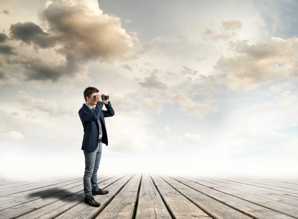 A man with a binocular looking at something on a wooden floor and gray sky