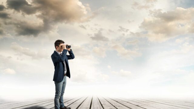 A man with a binocular looking at something on a wooden floor and gray sky