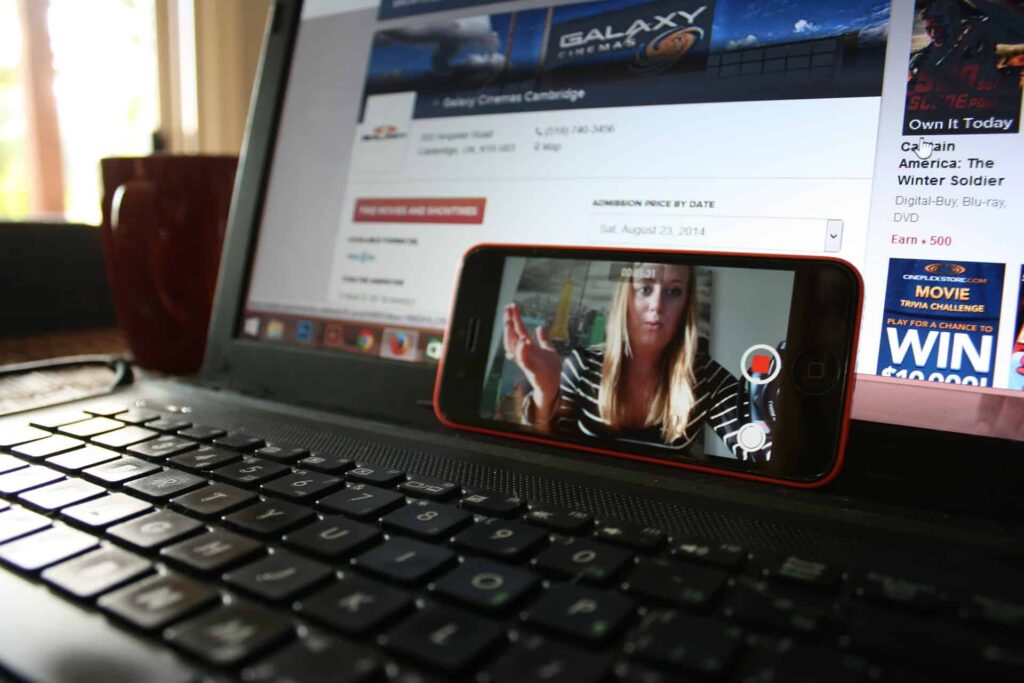 Smartphone propped on a laptop showing a video call, with a cinema website open in the background