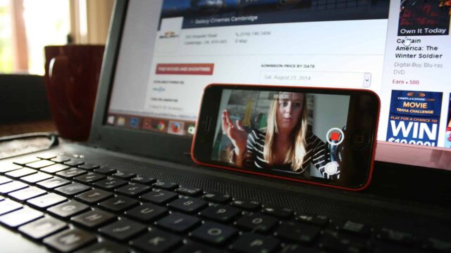 Smartphone propped on a laptop showing a video call, with a cinema website open in the background
