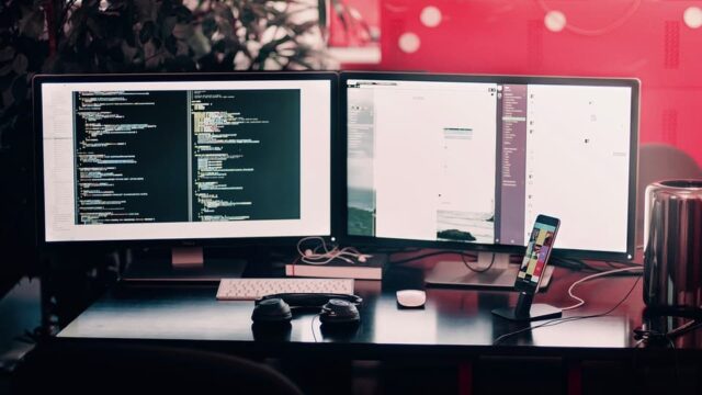 Dual-monitor developer workstation showing code on the left screen and a website design on the right, with headphones in the foreground