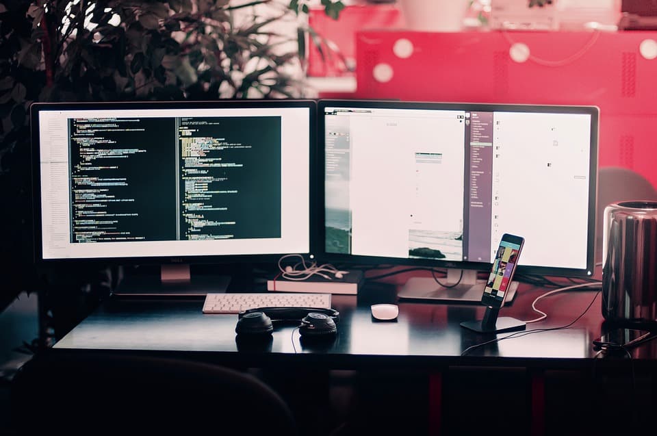 Dual-monitor developer workstation showing code on the left screen and a website design on the right, with headphones in the foreground