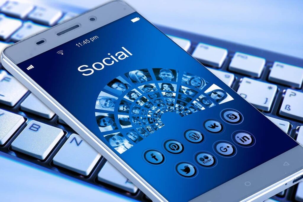 Smartphone resting on a keyboard displaying a social media app with platform icons including Twitter and LinkedIn