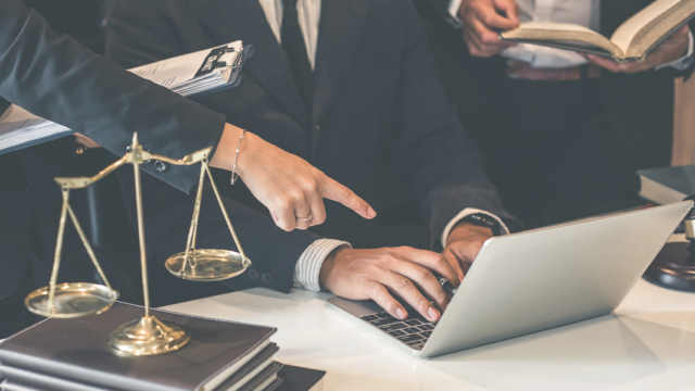 Two lawyers at a desk with a laptop and scales of justice, illustrating Google Ads for law firms
