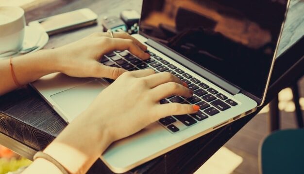 Woman typing on a laptop at a cafe table, illustrating B2B blogging and content creation