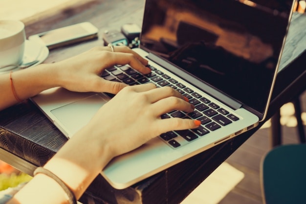 Woman typing on a laptop at a cafe table, illustrating B2B blogging and content creation