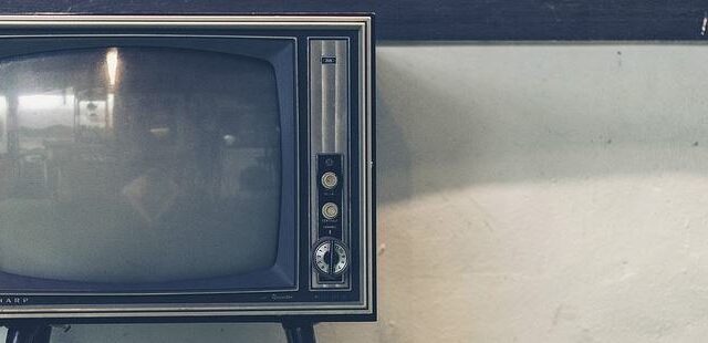 Vintage CRT television set against a plain wall, representing traditional advertising media