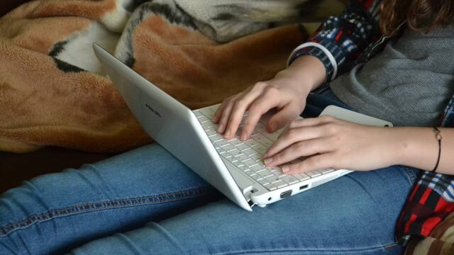 Person typing on a white laptop while sitting on a sofa, representing web development work