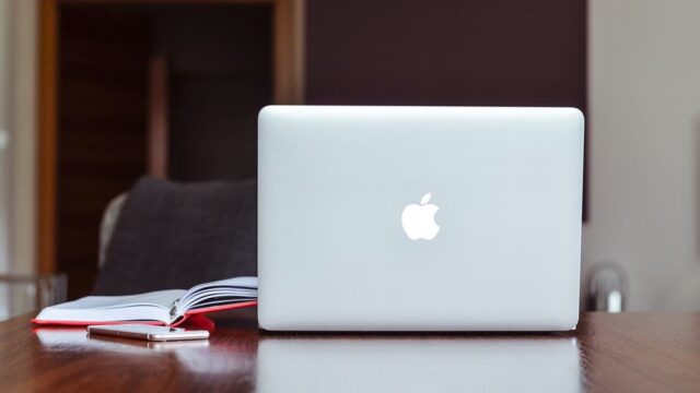 Apple MacBook on a wooden desk beside a notebook and smartphone, representing building a stronger online brand