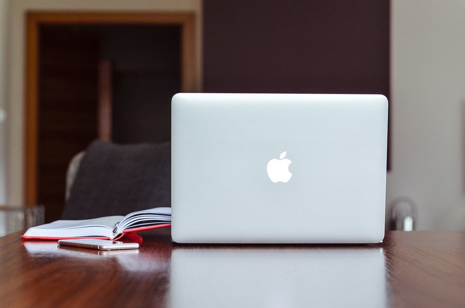 Apple MacBook on a wooden desk beside a notebook and smartphone, representing building a stronger online brand