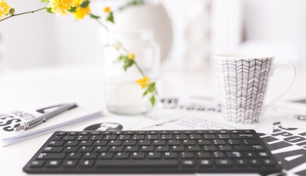 Keyboard, coffee mug, and yellow flowers on a white desk representing blogging and content creation