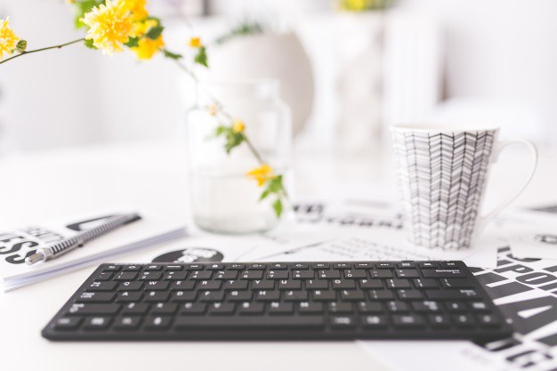 Keyboard, coffee mug, and yellow flowers on a white desk representing blogging and content creation