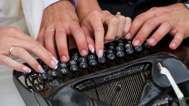 Two pairs of hands typing together on a vintage typewriter keyboard