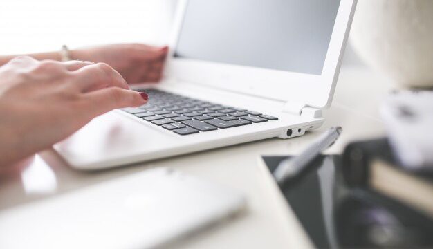 Woman typing on a white MacBook Air at a bright, minimal desk
