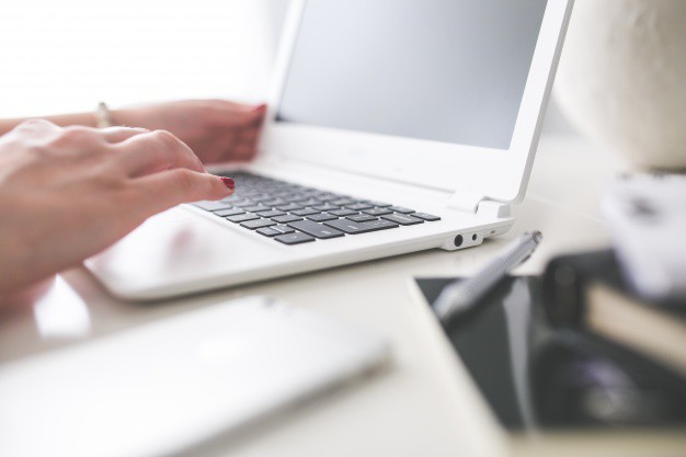 Woman typing on a white MacBook Air at a bright, minimal desk