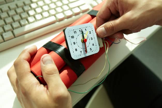 Hands holding a red dynamite bundle with a clock timer next to a computer keyboard