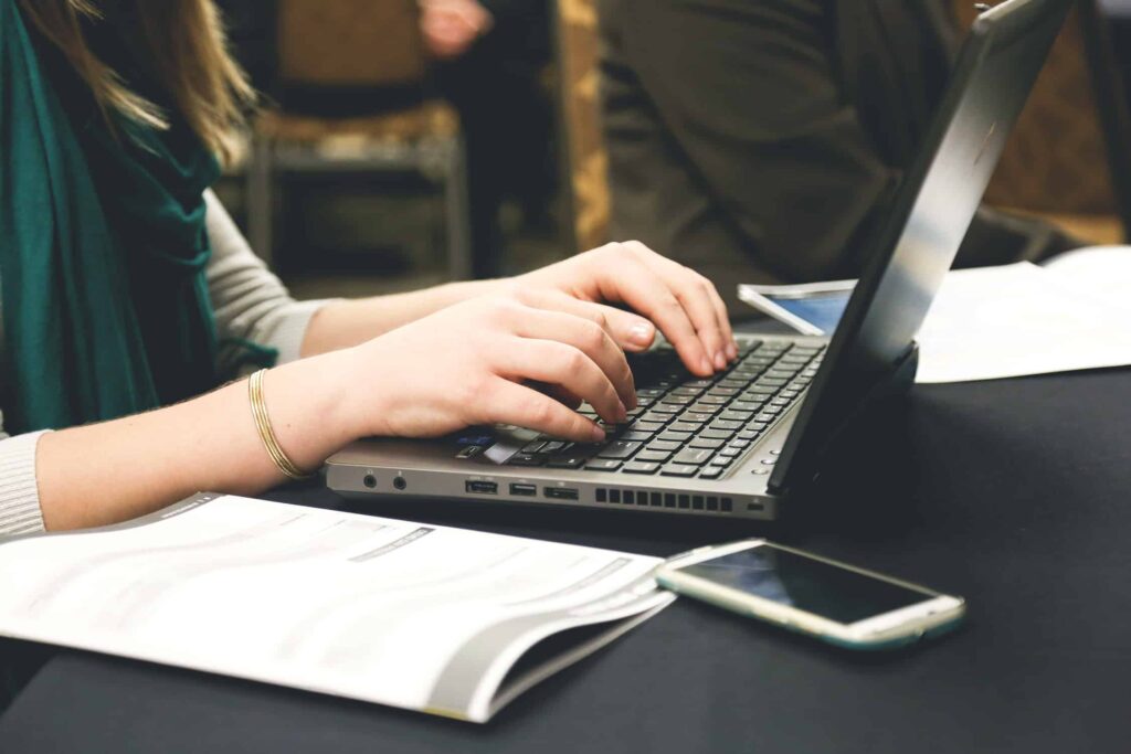 Woman typing on a laptop at a desk with documents and a smartphone nearby, representing online review management