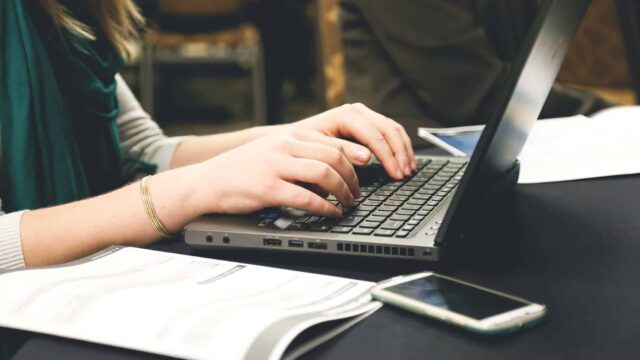 Woman typing on a laptop at a desk with documents and a smartphone nearby, representing online review management
