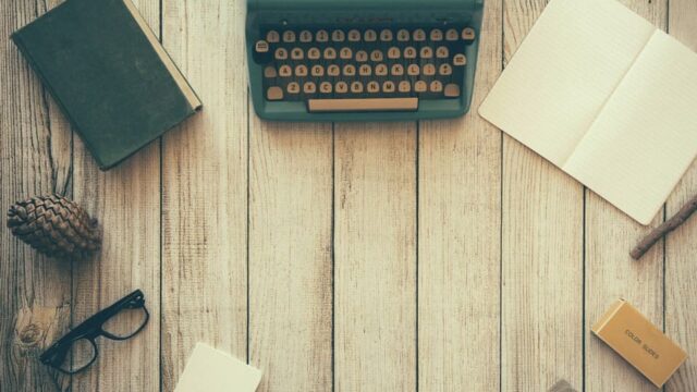 Vintage typewriter, open notebook, glasses and stationery laid out on a wooden desk, representing copywriting