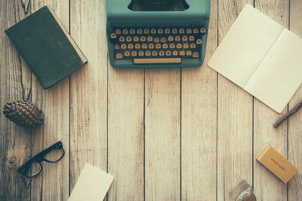 Vintage typewriter, open notebook, glasses and stationery laid out on a wooden desk, representing copywriting