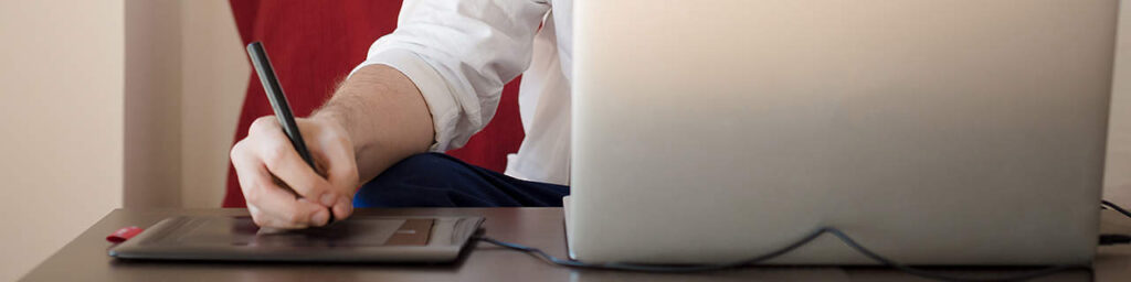 Designer using a stylus on a graphics tablet beside a laptop, illustrating continuous web design improvement