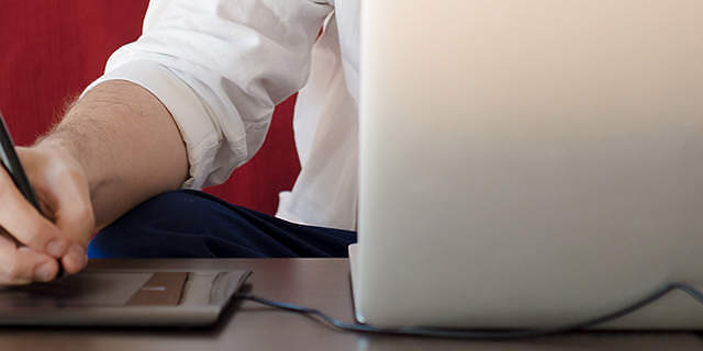 Designer using a stylus on a graphics tablet beside a laptop, illustrating continuous web design improvement