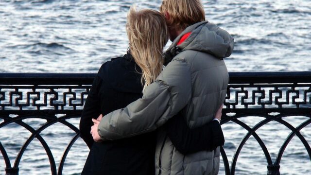 Couple embracing by a waterfront railing, illustrating the pros and cons of working with a significant other