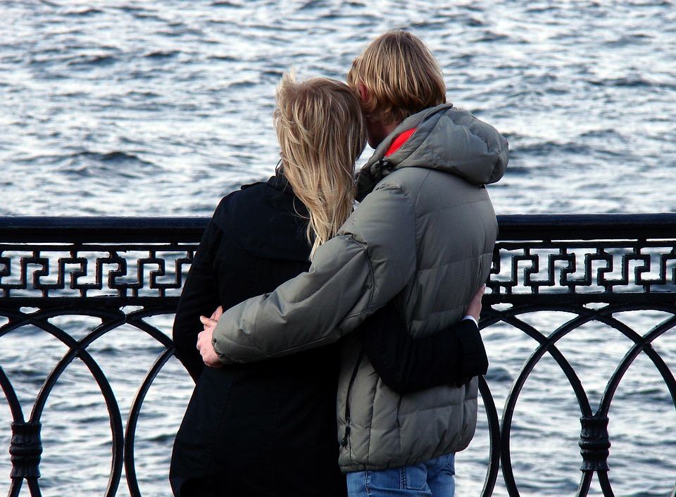 Couple embracing by a waterfront railing, illustrating the pros and cons of working with a significant other