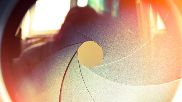 Close-up macro shot of a camera aperture with warm orange light shining through the lens blades