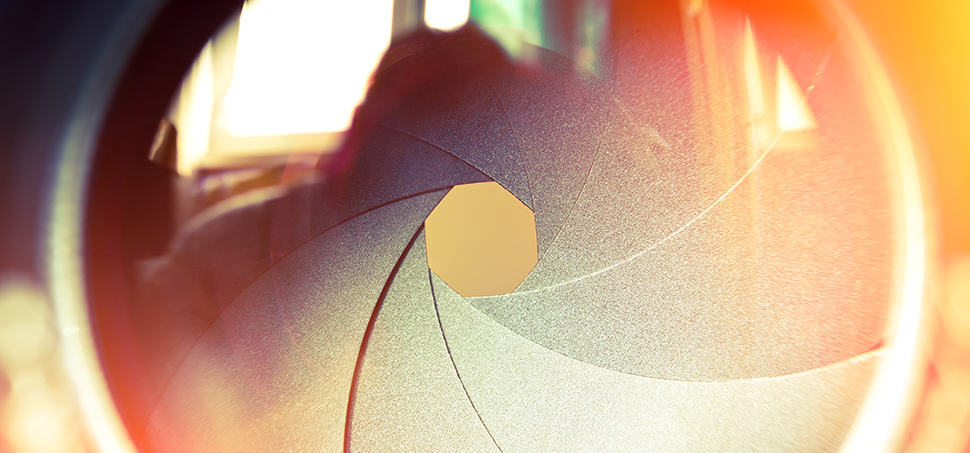 Close-up macro shot of a camera aperture with warm orange light shining through the lens blades