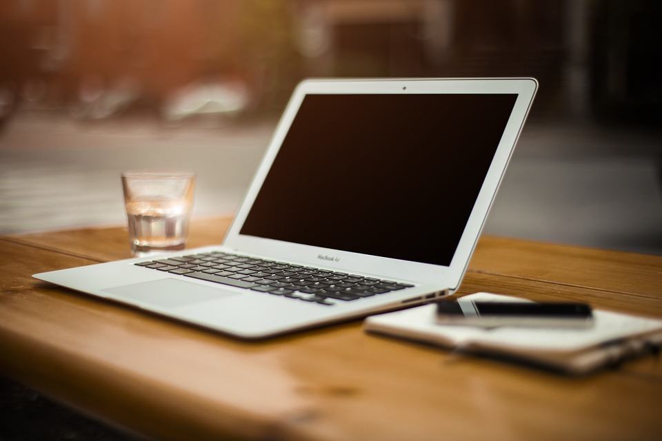 MacBook Air open on a wooden table beside a glass of water and a notebook, representing blogger outreach tools