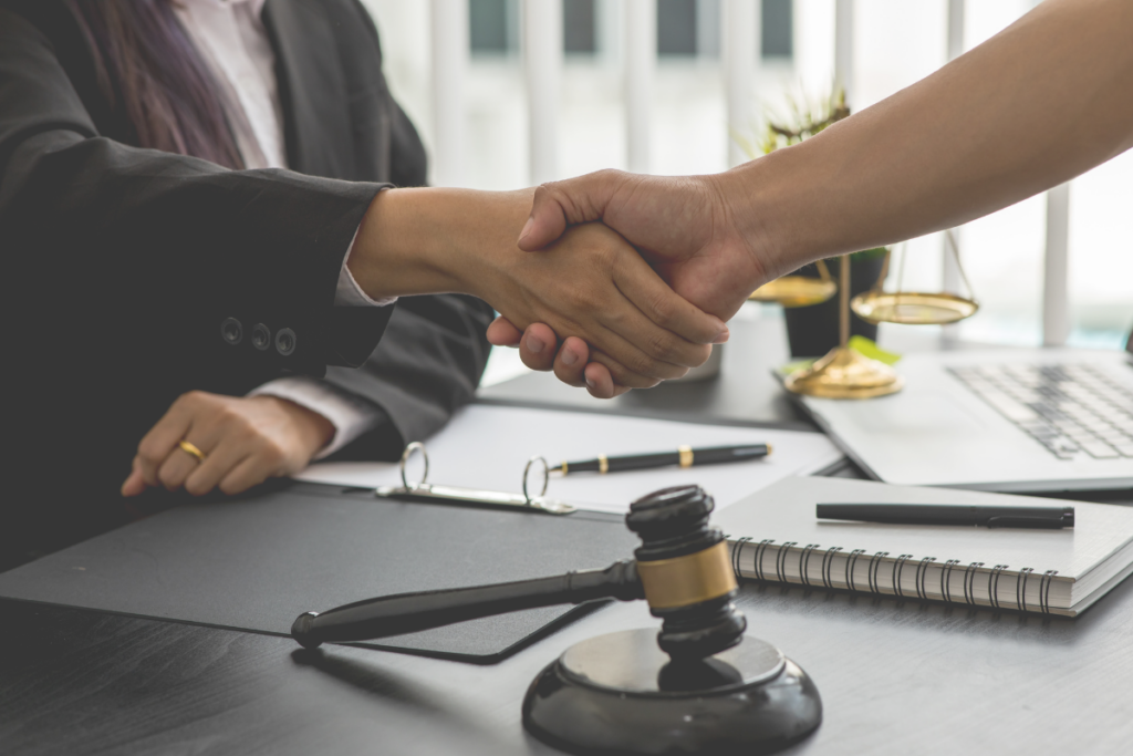 Two professionals shaking hands at a desk with gavel and scales of justice, representing legal client relationships
