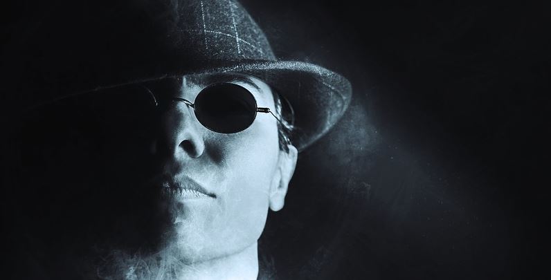 Moody black and white portrait of a man in a fedora and sunglasses, illustrating project management lessons from a gangster