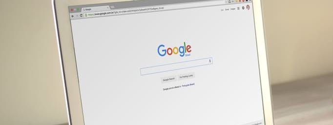 Laptop with Google homepage open on screen, angled side view on a light surface