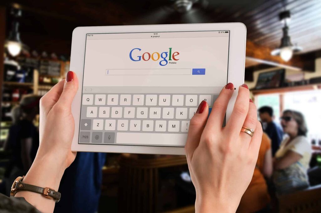 Woman using both hands to type on an iPad showing Google search homepage with on-screen keyboard