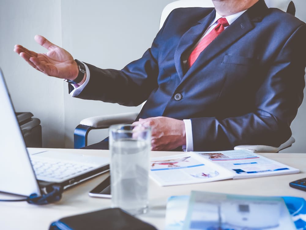 Business professional in a suit gesturing at a desk with reports and a laptop, illustrating thought leadership in your industry