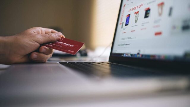 Person holding a credit card toward an open laptop showing an ecommerce store with discount offers