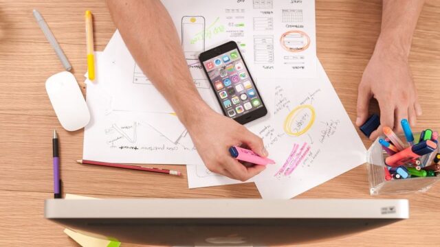 Overhead view of a person planning a keyword strategy with a smartphone, wireframe sketches and highlighters on a desk