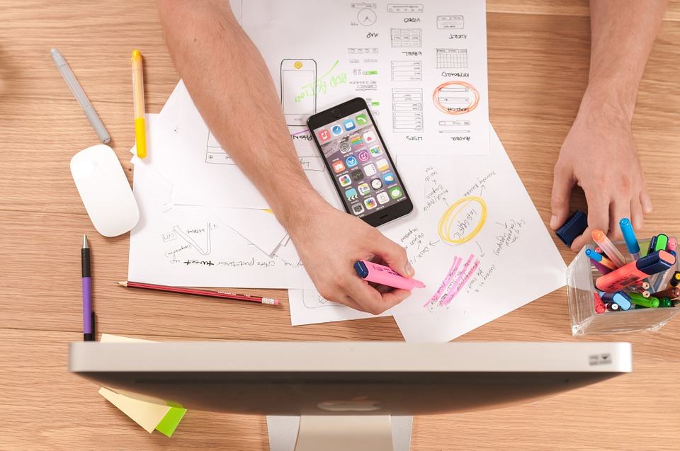 Overhead view of a person planning a keyword strategy with a smartphone, wireframe sketches and highlighters on a desk