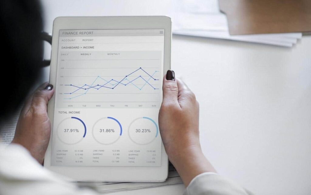 Person holding a tablet displaying a finance report dashboard with line charts and donut charts showing income data