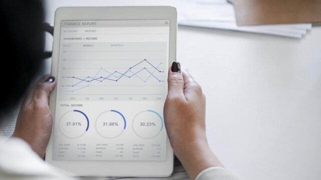 Person holding a tablet displaying a finance report dashboard with line charts and donut charts showing income data