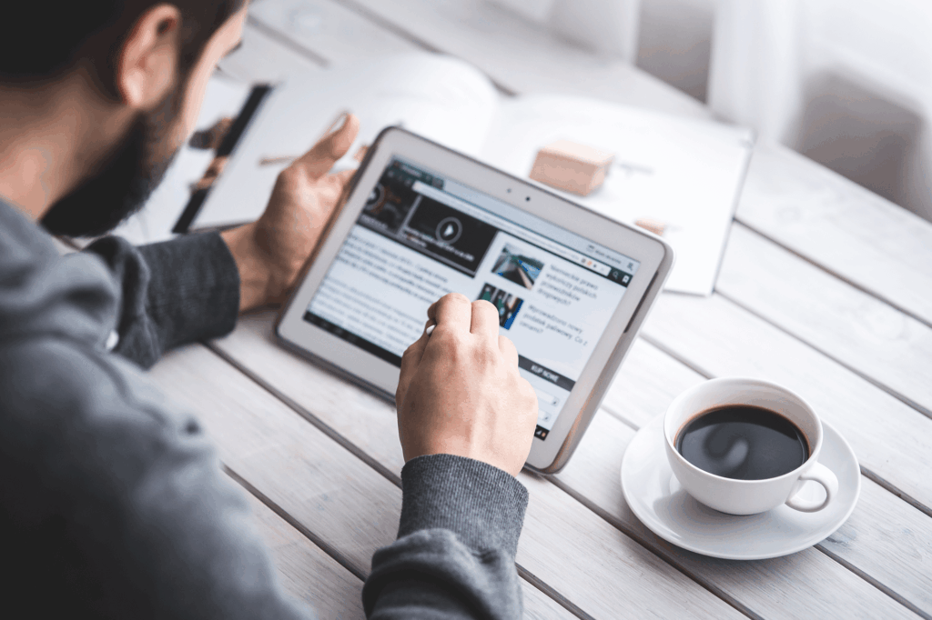 Man reading a news website on a tablet with a coffee cup beside him, illustrating digital content research