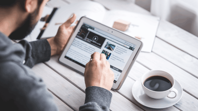 Man reading a news website on a tablet with a coffee cup beside him, illustrating digital content research