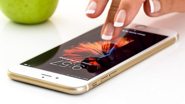 Hand tapping the screen of a gold iPhone lying flat on a white surface, illustrating mobile-first design