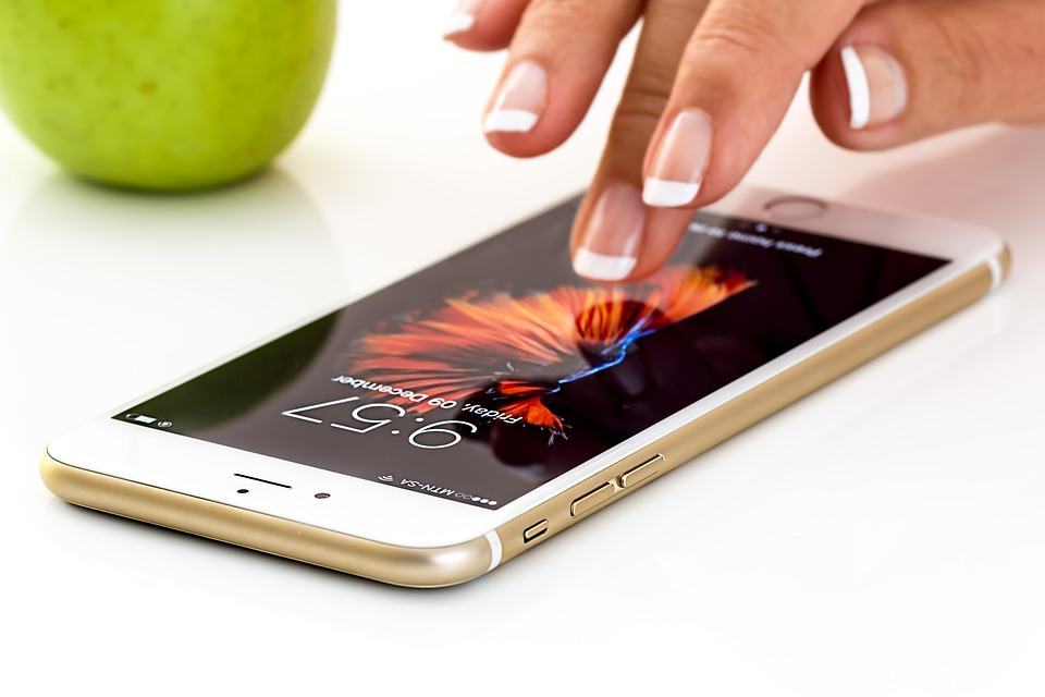 Hand tapping the screen of a gold iPhone lying flat on a white surface, illustrating mobile-first design